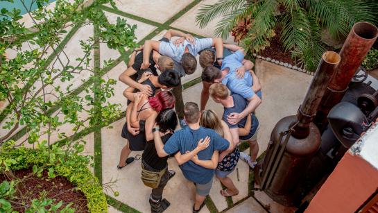 group of people in a circle, holding their arms and looking down