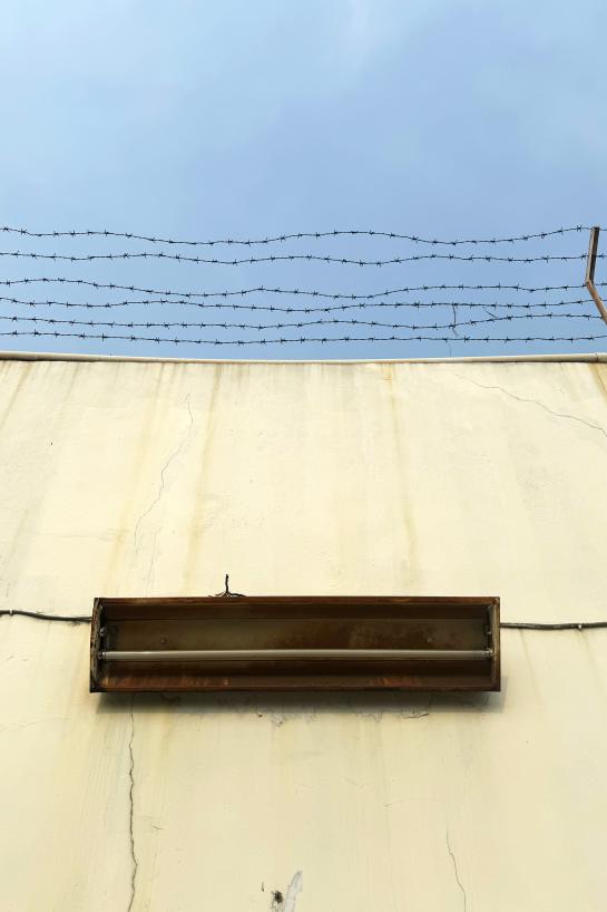 yellow concrete wall with barbed wire and old neon lamp against gloomy blue sky