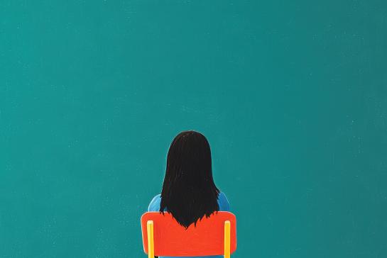 A woman sits in a yellow chair in front of a blue wall 