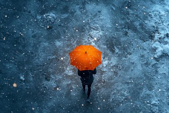 Woman walking alone with orange umbrella, snowy street, night 