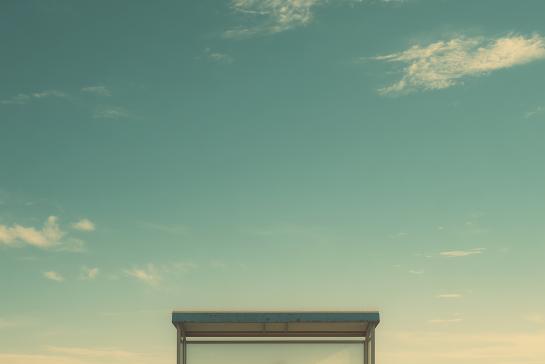 Lonely woman standing at rural bus stop in wide open field under clear sky
