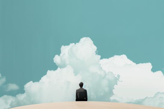 Businessman sitting on the top of a sand dune with clouds in the sky. 