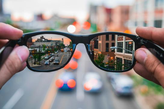 Hands holding sunglasses that sharpen the view of the city street