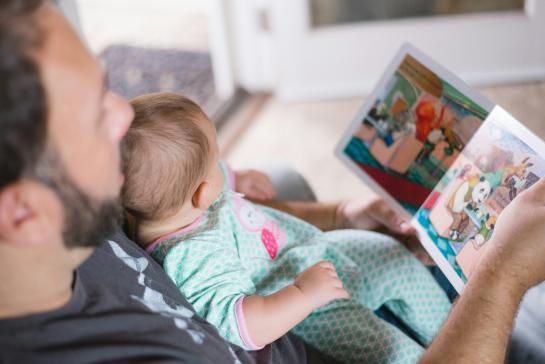 A male reading to a baby on his knees