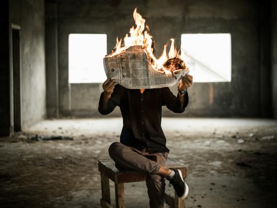 Man sitting on a chair and reading a burning newspaper