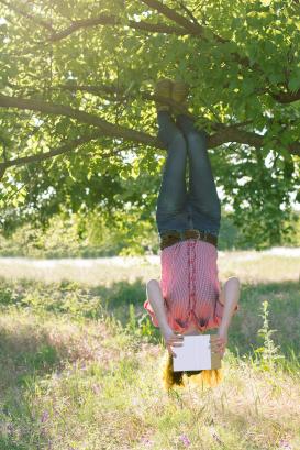 A girl hanging head down from the tree and reading a book