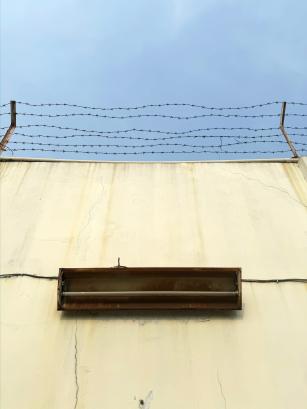 yellow concrete wall with barbed wire and old neon lamp against gloomy blue sky