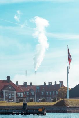 Industrial pipes of the plant emit smoke into the sky against the background of an old beautiful Scandinavian Palace in Denmark