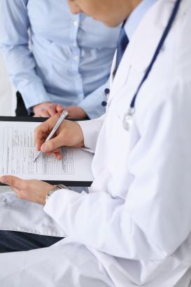 Male doctor holding application form while consulting female patient in hospital. 