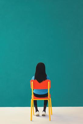 A woman sits in a yellow chair in front of a blue wall 