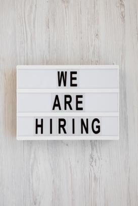'We are hiring' words on a lightbox on a white wooden surface, overhead view. 