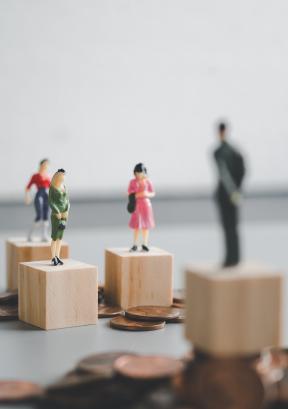 miniature man and woman stand on coin stacks 